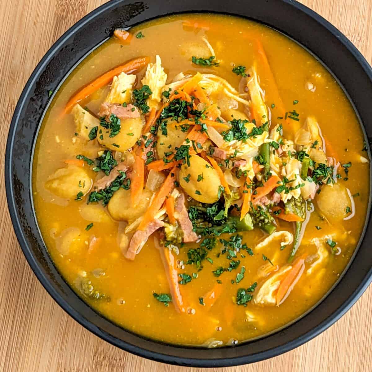 Hearty pumpkin gnocchi chicken soup in a black bowl on a rustic wooden background.